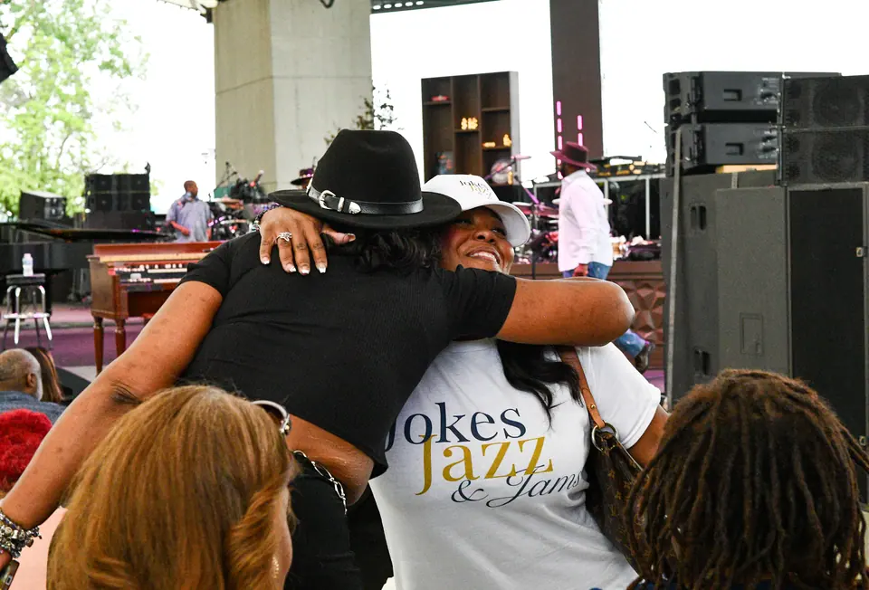 A guest in a Jokes, Jazz & Jams shirt hugging a friend
